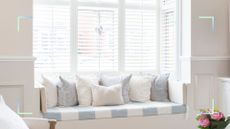 White room with a window seat with white shutter and a blue and white stripe cushion