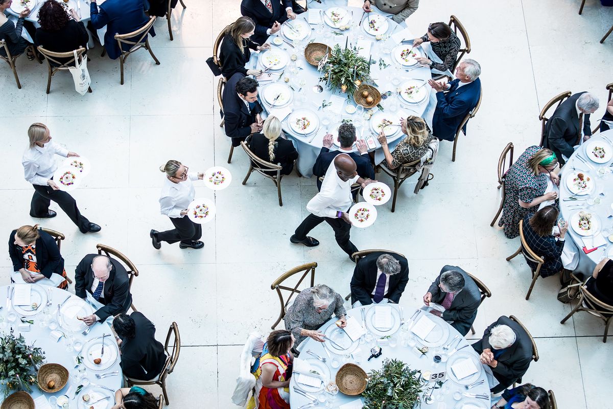 Photograph titled Three Waiters, taken by Clare Hannan. It shows three waiters weaving their way through seated guests with starter plates during dinner service at The British Museum in London, UK.