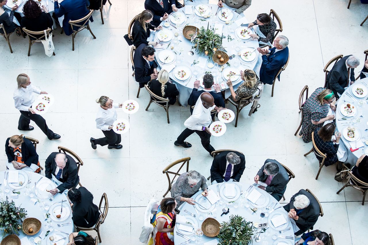 Photograph titled Three Waiters, taken by Clare Hannan. It shows three waiters weaving their way through seated guests with starter plates during dinner service at The British Museum in London, UK.