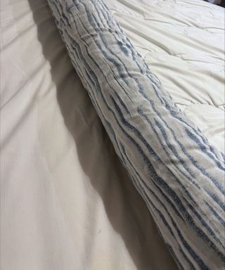 A white comforter being rolled up with a blue and gray patterned duvet cover with a pale gray sheet underneath