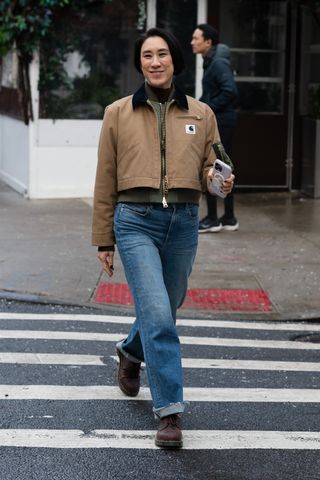 A woman crossing the street in jeans and a work jacket