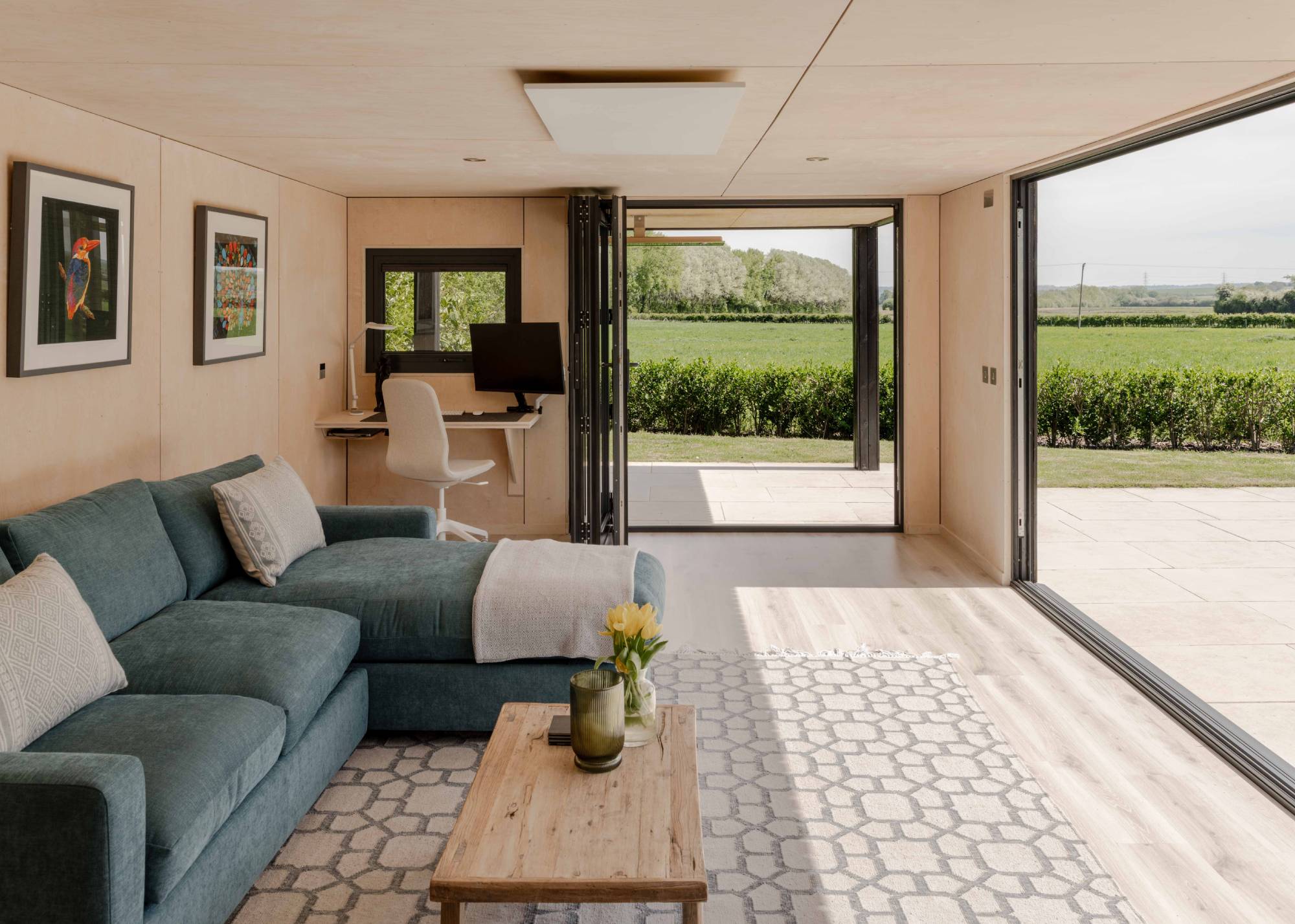 modern interior of garden room with large open bifold doors, a desk and blue sofa