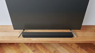 The Sony HT-SF150 soundbar positioned on a wooden cabinet, between the feet of a TV