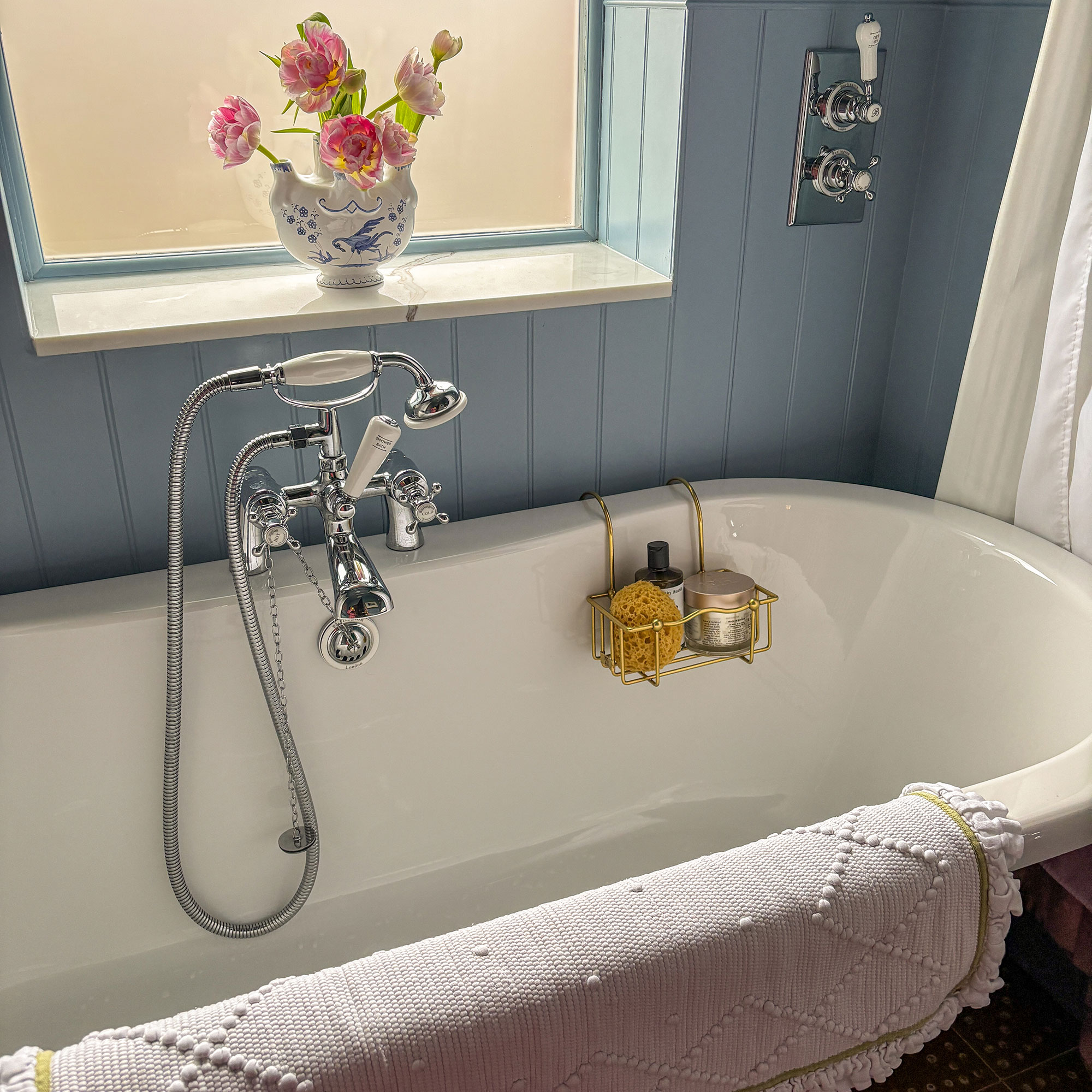 Traditional roll-top bath in panelled bathroom with vase of flowers on windowsill