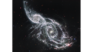 two swirling galaxies in deep space glow in shades of red and yellow