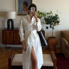 Woman wears white shirt dress with tie belt, black bag