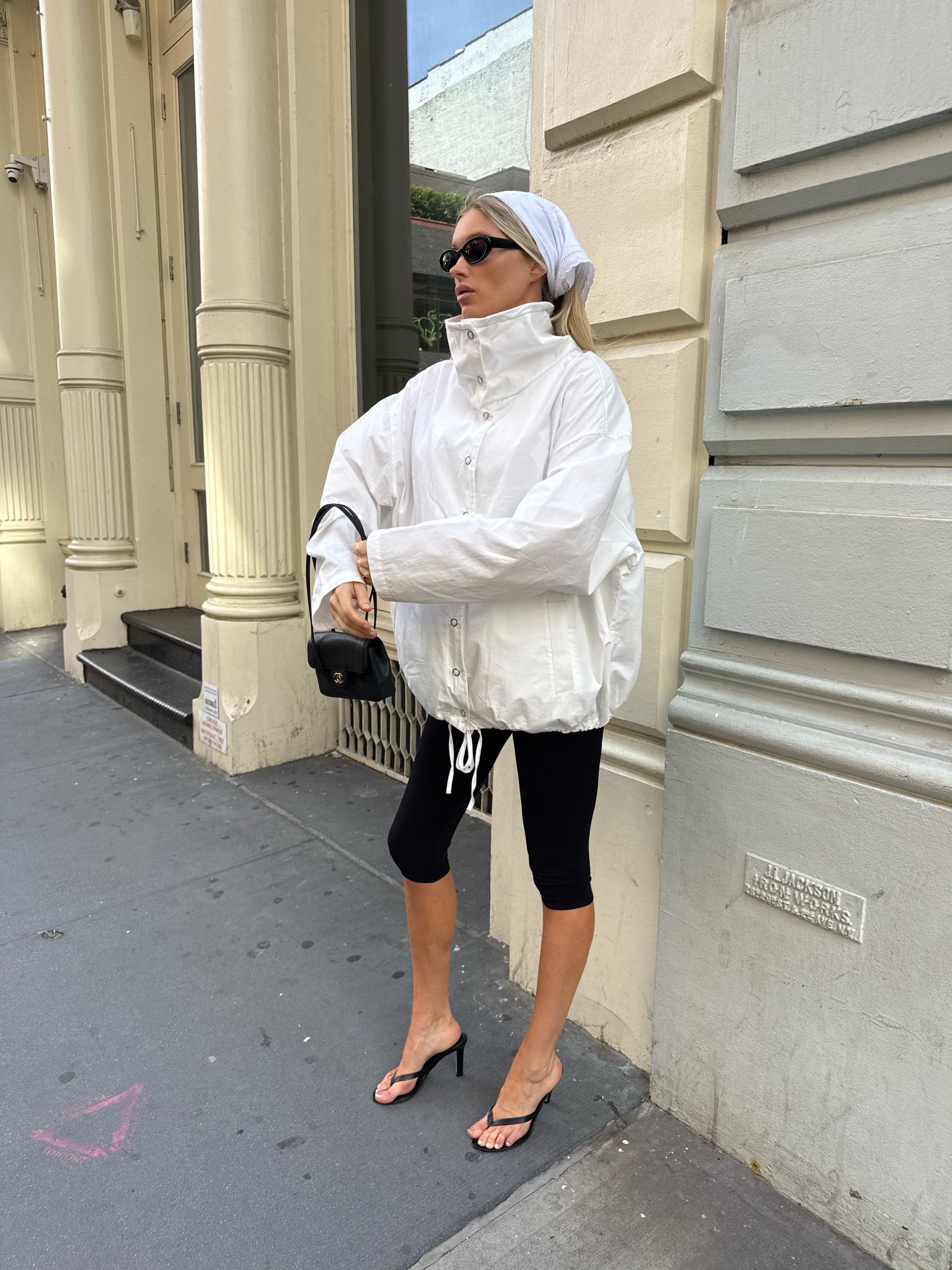 Elsa Hosk wears black capri pants with black heeled flip-flops and a white high-neck jacket.