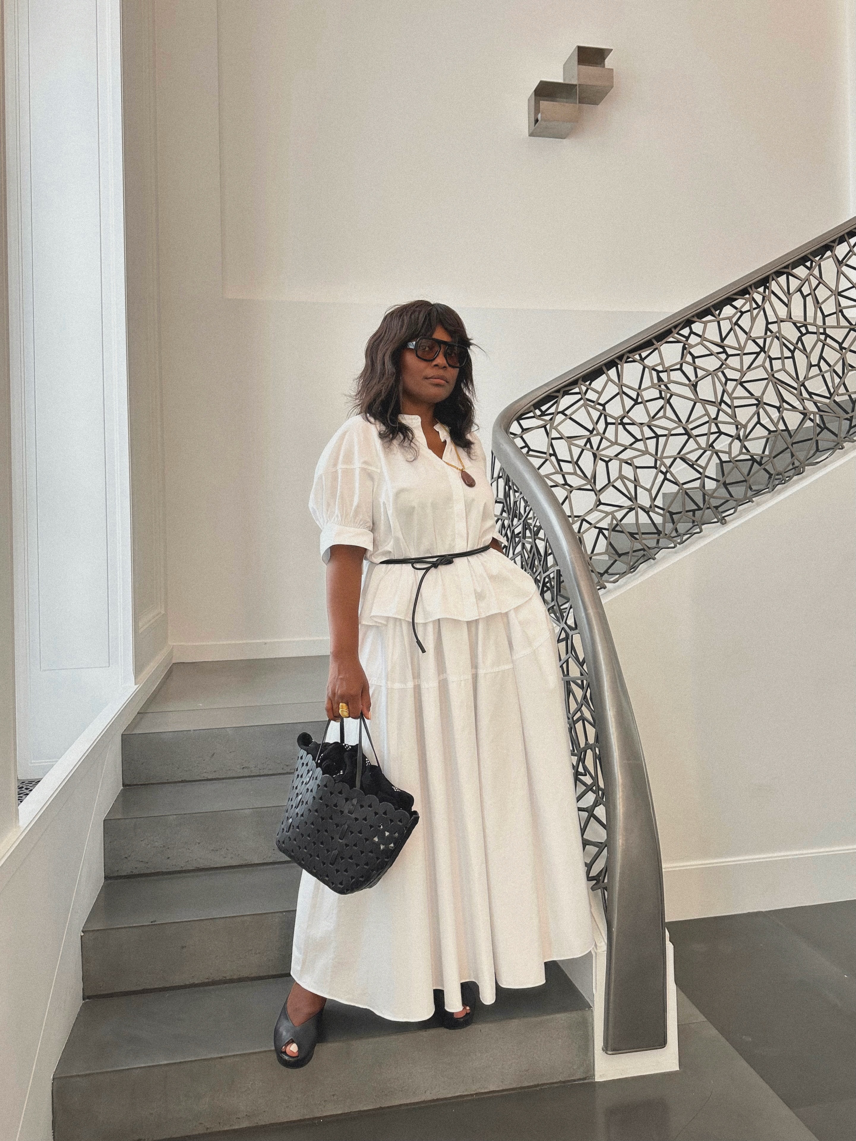 An image of an influencer on a staircase wearing a white puff-sleeve blouse, white skirt and black peep-toe heels in Paris