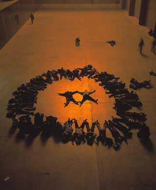 A group of people lying down in the shape of a circle with two people lying down inside the circle.
