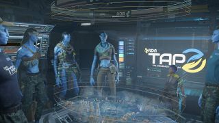 Still from the video game Avatar: Frontiers of Pandora. Five Na'vi (tall, blue humanoids with long dark hair) and one human female (half their size) are all gathered around a futuristic, holographic map. In the background there is a large screen which reads RDA: TAP).