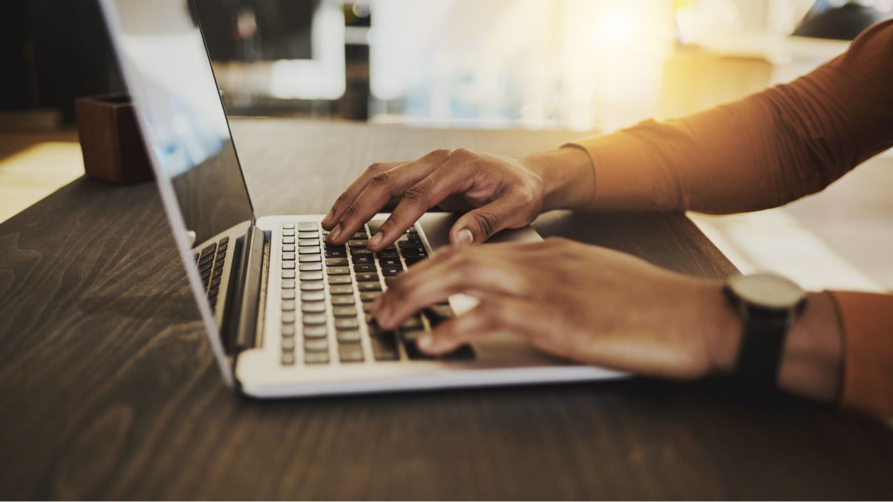 An adult types on a laptop, only their hands showing.