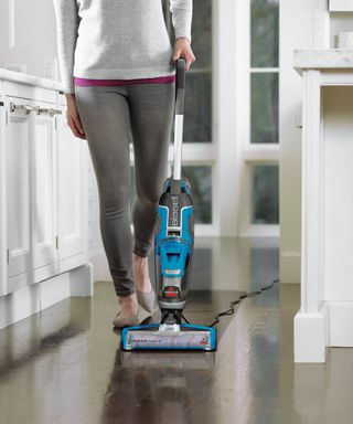 A woman wearing light grey jumper and grey denim jeans demonstrating how to use a BISSELL Crosswave 3-in-1 carpet, rug and hard floor cleaner