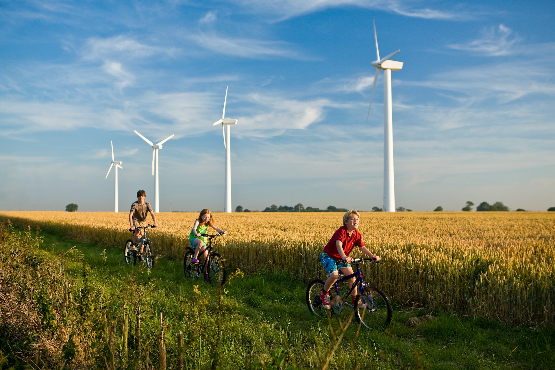 Crianças andando de bicicleta passando por turbinas eólicas