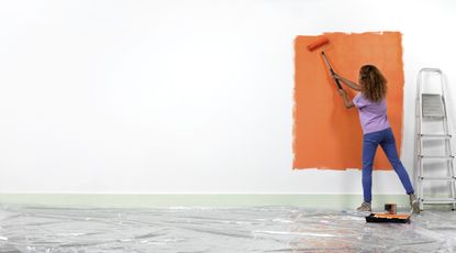 A person painting a wall orange with a roller.
