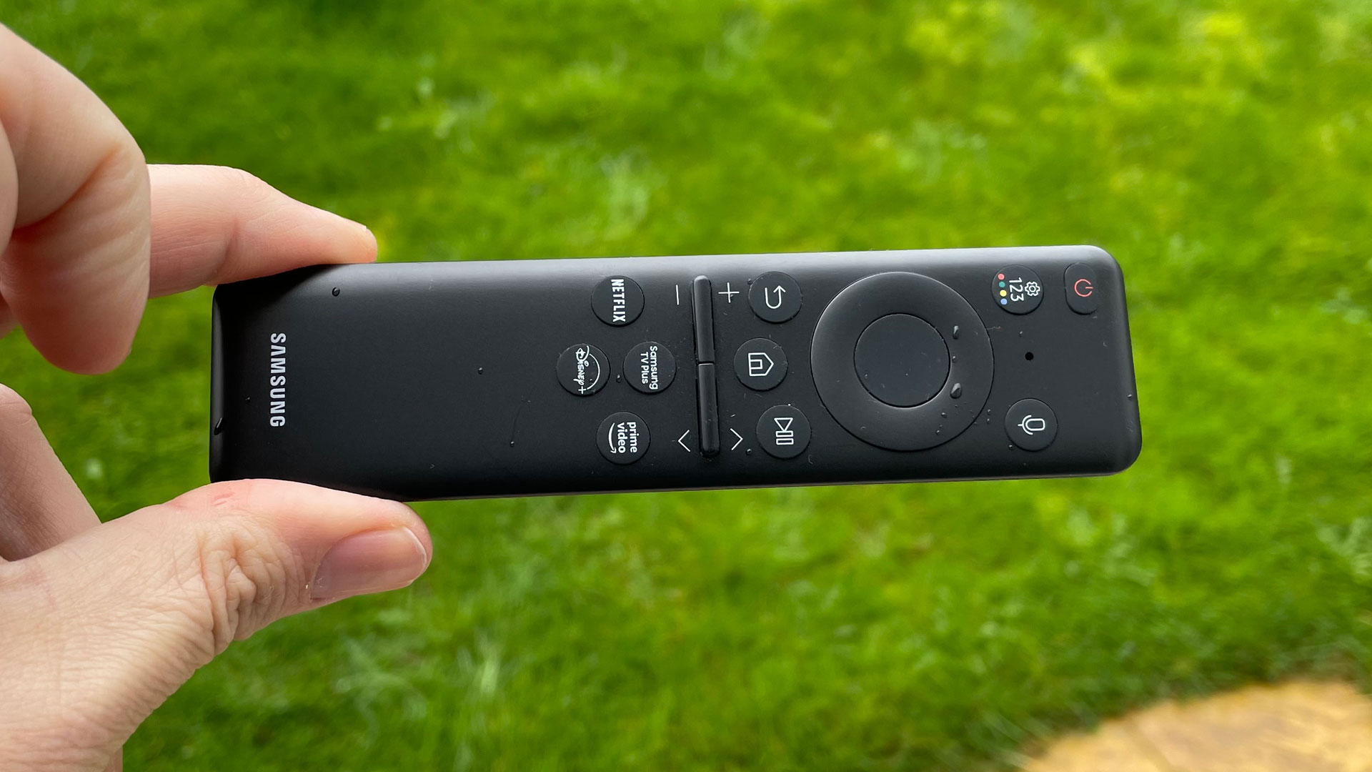 A hand holding the remote for the Samsung QN95C