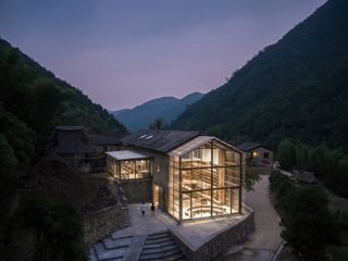 The Capsule Hotel and Bookstore is surrounded by mountains. The photo is taken at night and through the all-glass back part, we see a library.