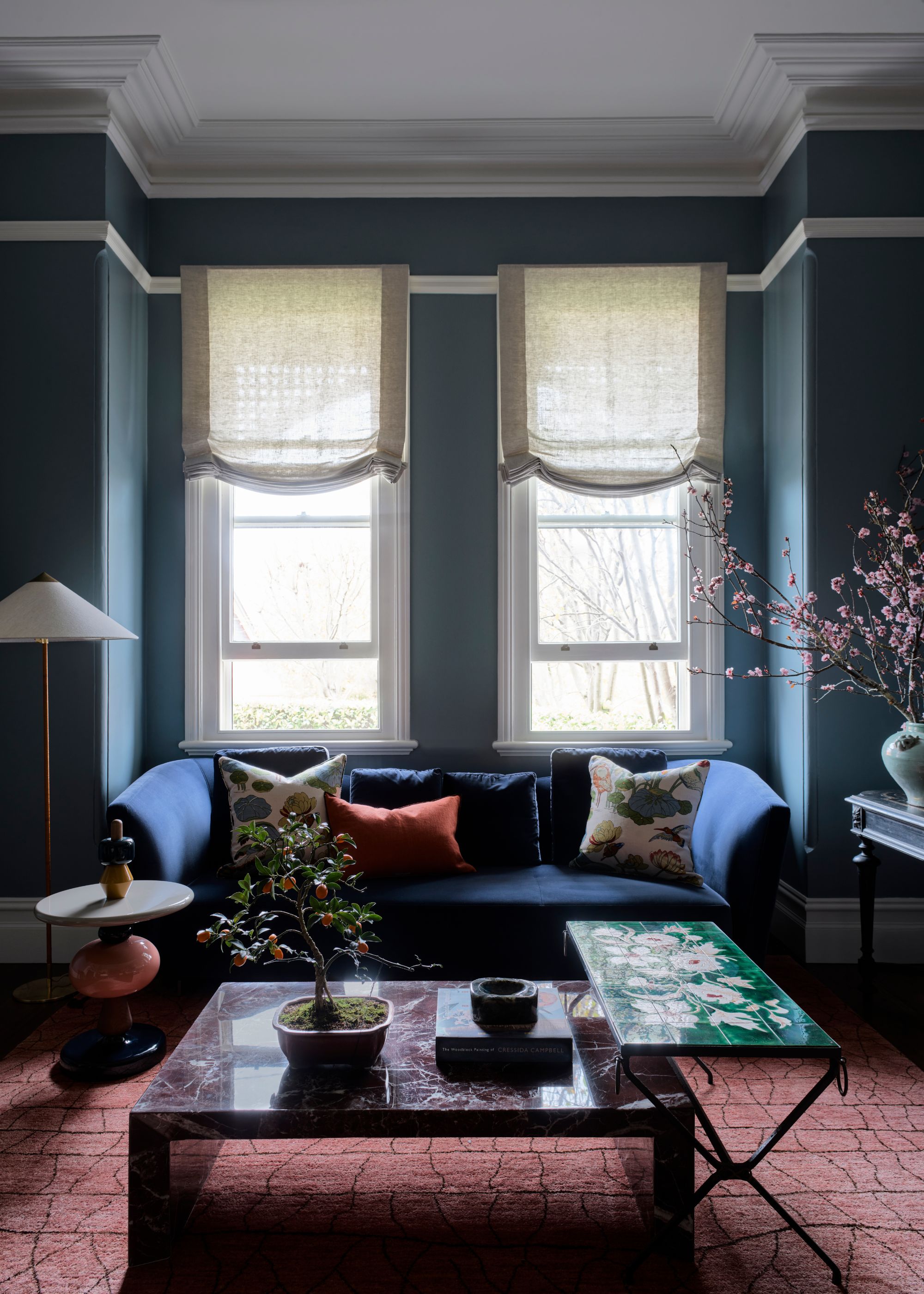 A blue painted living room with a blue sofa by the window. There is a large red carpet placed beneath the sofa