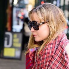 Jennifer Lawrence wearing a pale yellow coat, colorful scarf, La Ligne pants, Nike sneakers, and Dior sunglasses