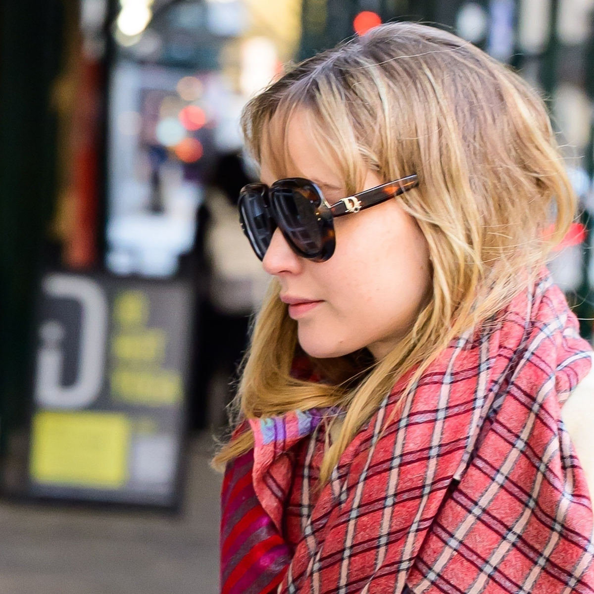 Jennifer Lawrence wearing a pale yellow coat, colorful scarf, La Ligne pants, Nike sneakers, and Dior sunglasses