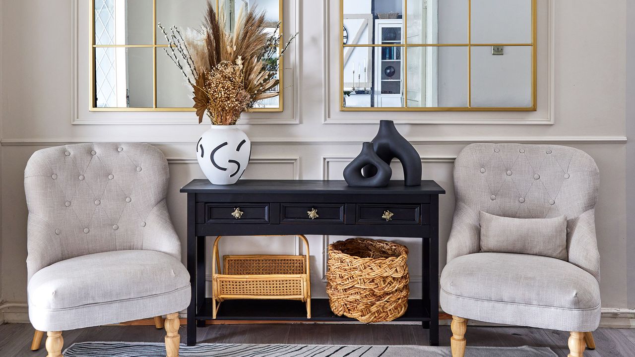 Two occasional chairs in a hallway with a black concole table and two gold grid-style mirrors