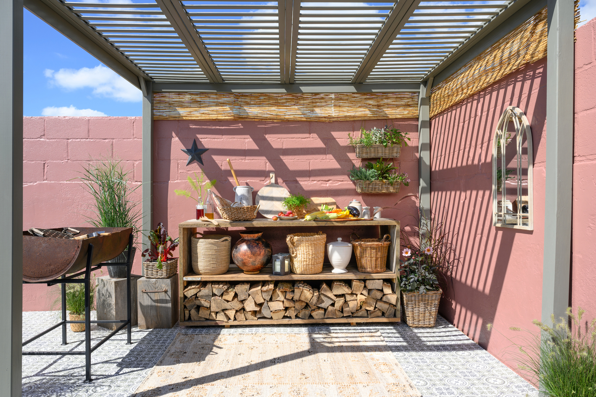 A walled garden with pink walls, a pergola, and an outdoor bench with integrated log storage