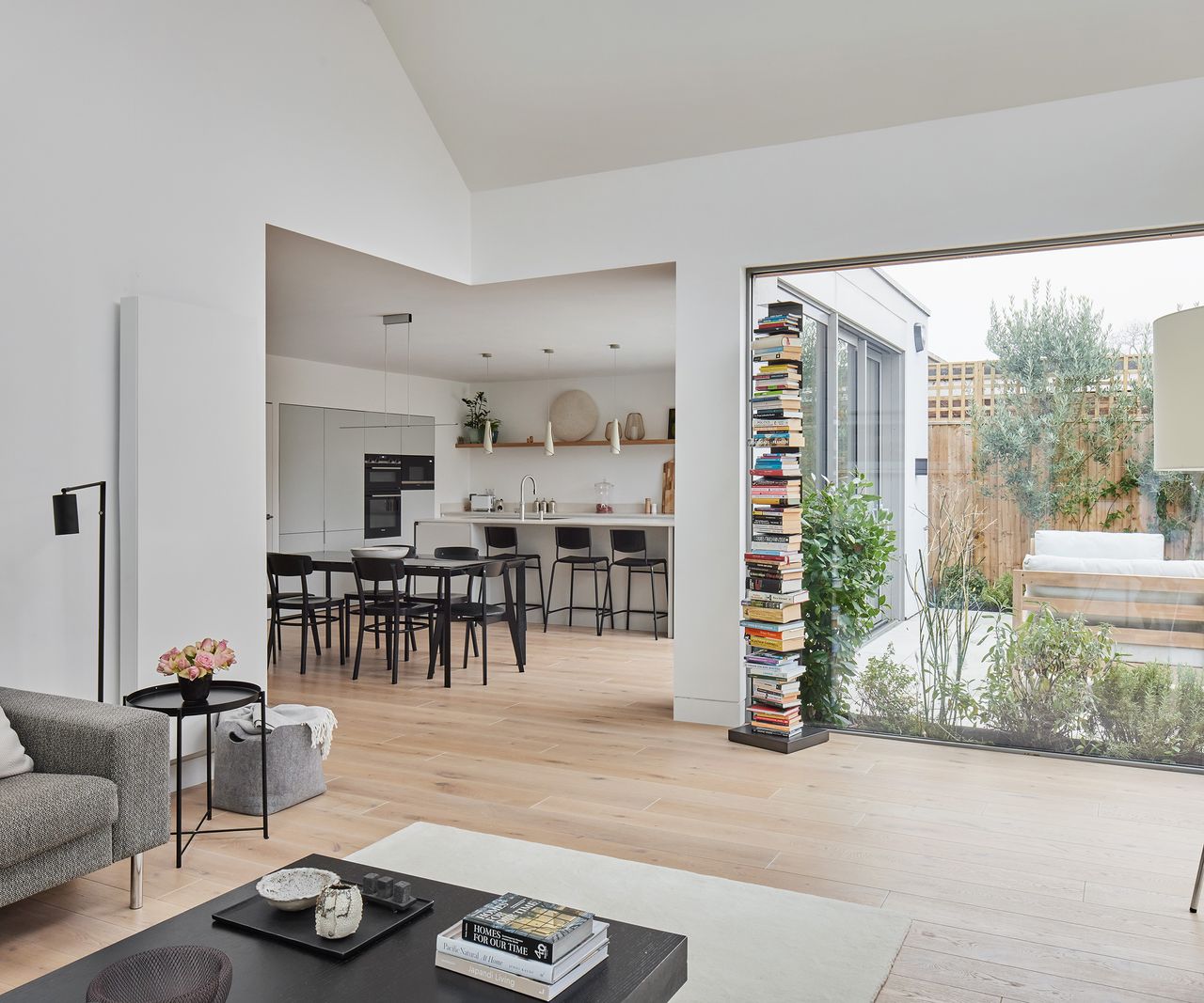 An open plan living area looking into a kitchen and dining room with a large glass floor to ceiling window