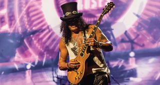 Slash of Guns N' Roses wears his trademark top hat as he takes a solo on his Gibson Les Paul – the stage is lit up in purple and white in the background.