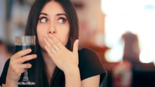 woman holds a glass of wine and covers her mouth as if she just hiccuped