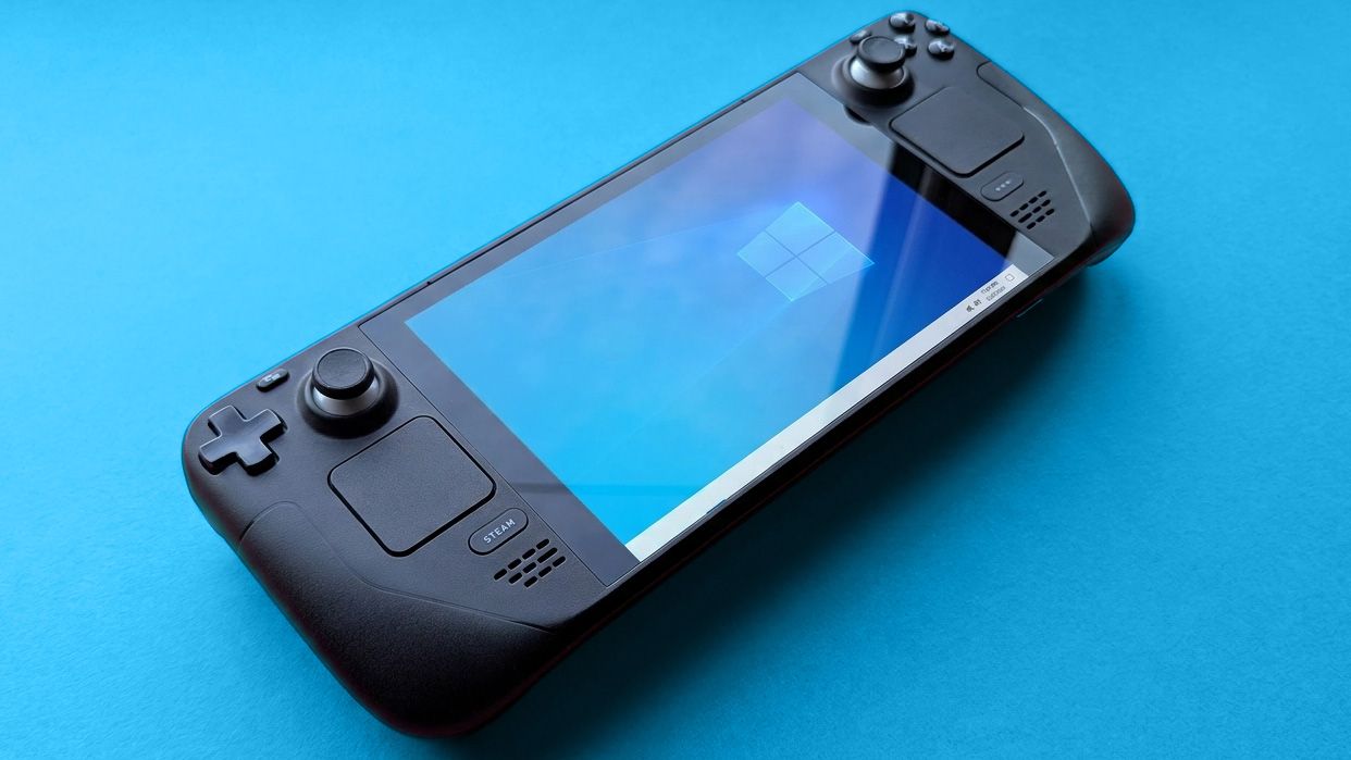 Steam Deck handheld gaming console with a black design is displayed against a blue background. The screen shows a blue Windows logo wallpaper