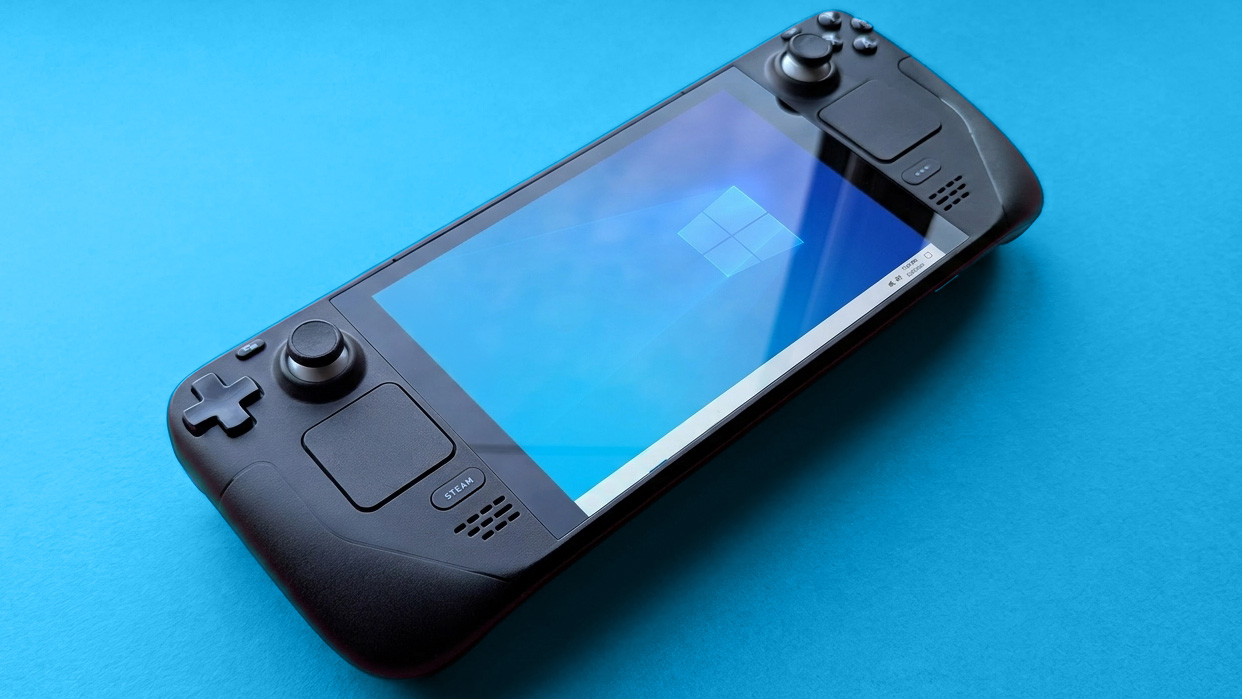 Steam Deck handheld gaming console with a black design is displayed against a blue background. The screen shows a blue Windows logo wallpaper