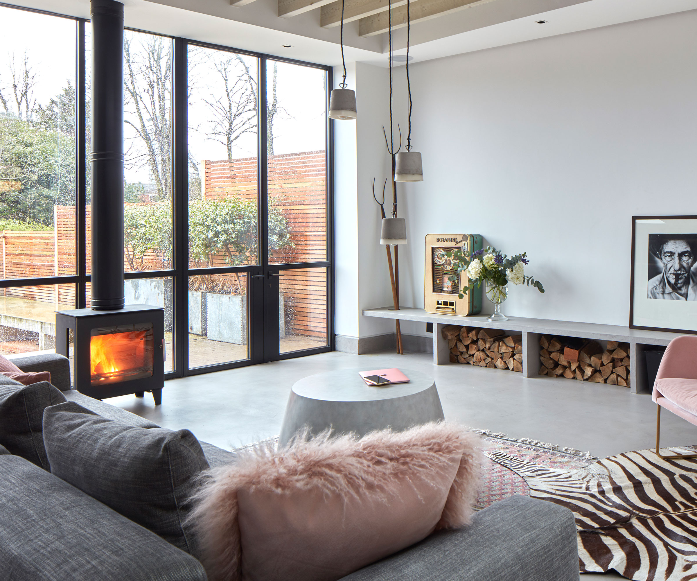 contemporary living room with log burning stove and polished concrete flooring with full height glazing