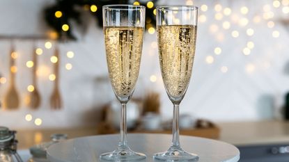 Champagne glasses filled with champagne in the foreground with twinkle lights in the background