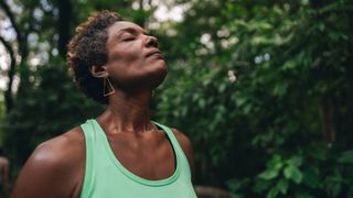 Woman doing outdoor meditation, eyes closed, looking up at the trees