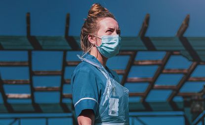NHS nurse in PPE standing against blue sky