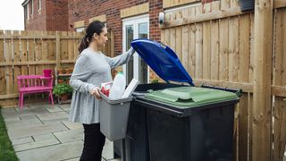 Pregnant woman disposing of her household recycling into an outdoor bin in her garden