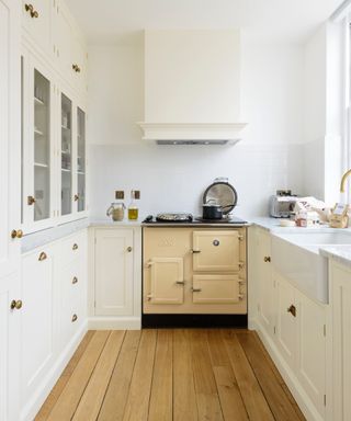 white kitchen with wooden floorboards, white cabinetry and gold effect hardware, cream Esse range,