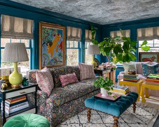 A family room with bright teal blue walls, and sofas, curtains and cushions in mismatched patterns and colors