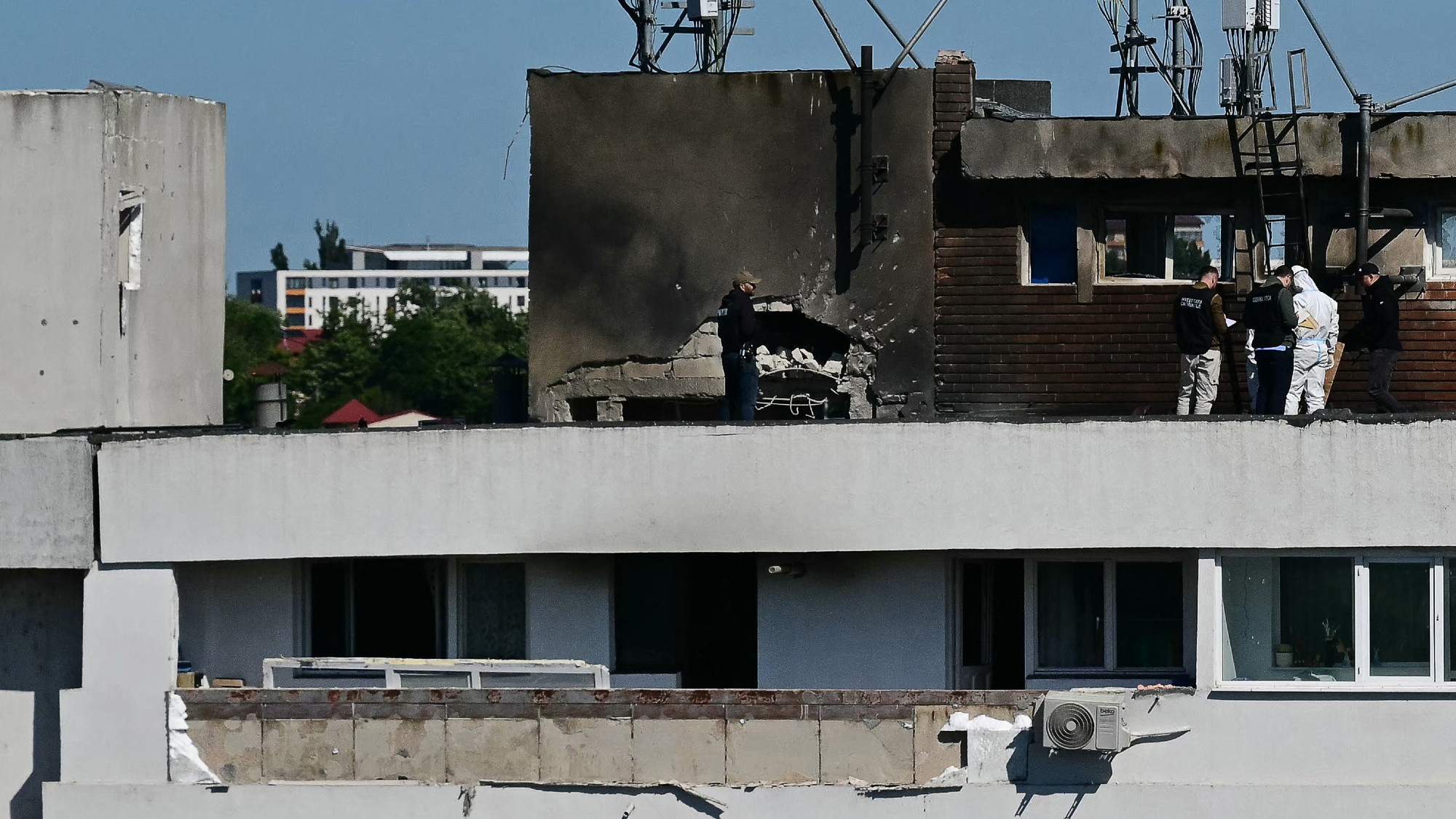 side shot of the roof of a building in Romania hit by a Russian drone strike. a trip of investigators are investigating near the strike site