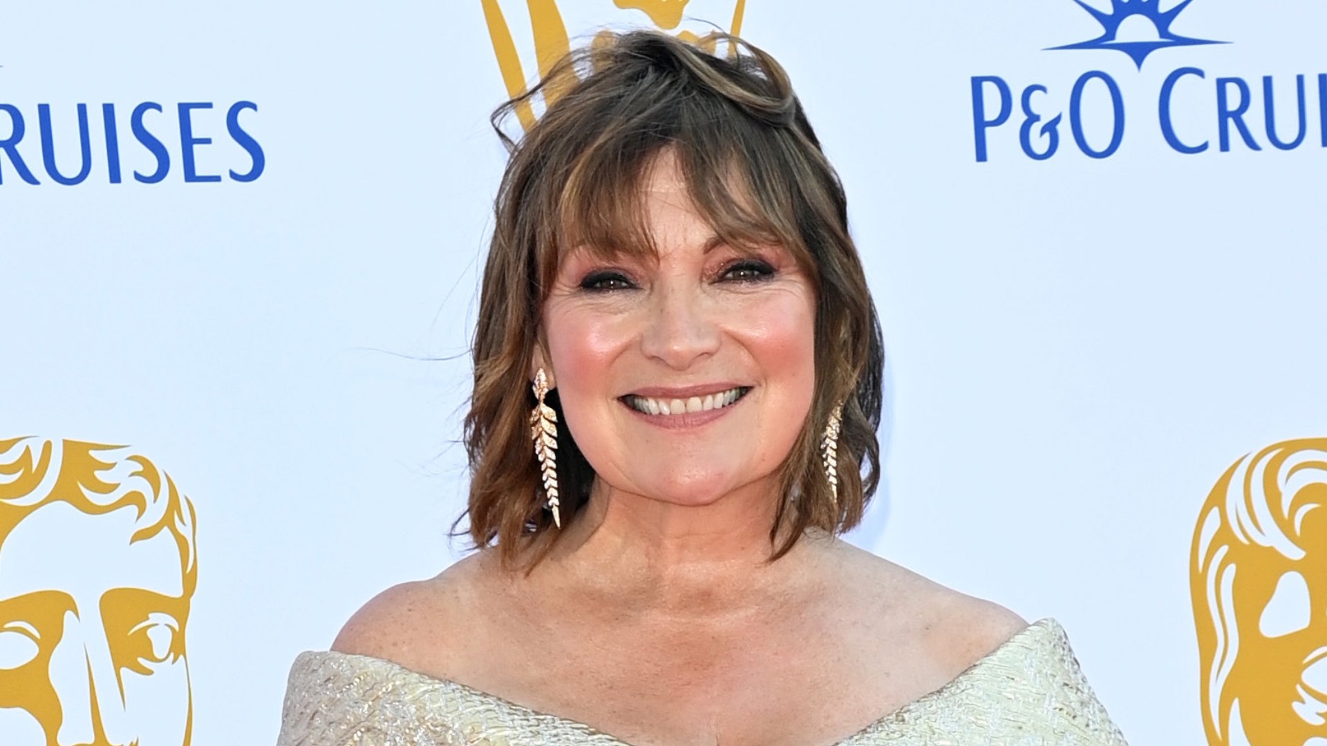 Image of Lorraine Kelly smiling with curled brunette bob and wearing an off the shoulder gold gown
