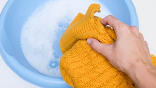An orange sweater ready to soak in a bowl filled with water and detergent