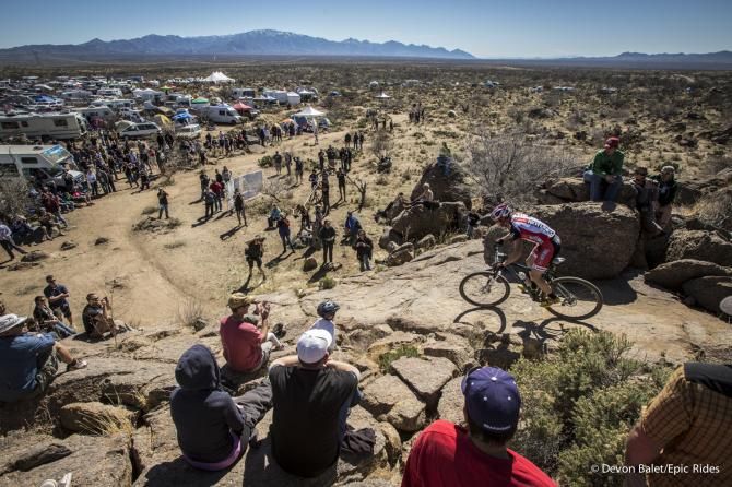 A Stans NoTubes rider approaches a rocky descent with many looking on