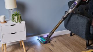 Shark PowerDetect cordless vacuum with headlamps illuminated, cleaning the edge of a room