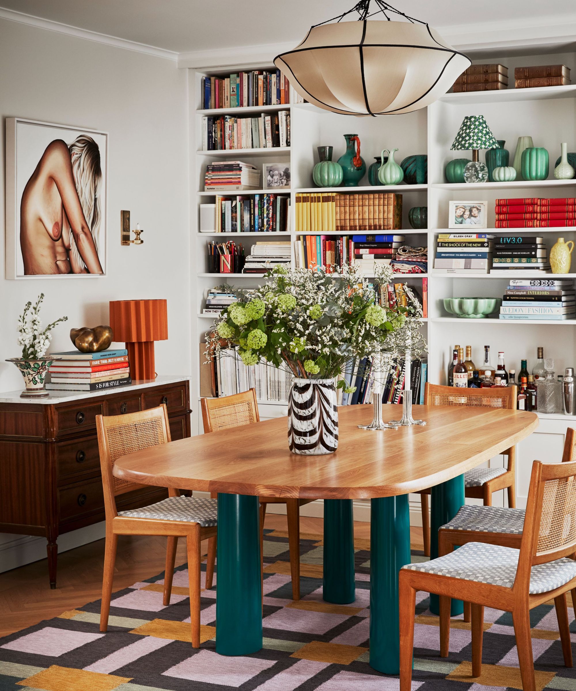 mid century dining room with green table legs and a full wall of styled shelves and statement art
