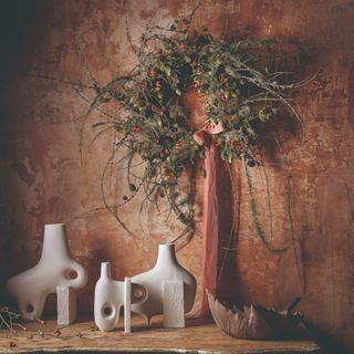 A wild, unruly Christmas wreath with berries and an oversized ribbon tied into a bow hanging on a limewash wall in a terracotta shade