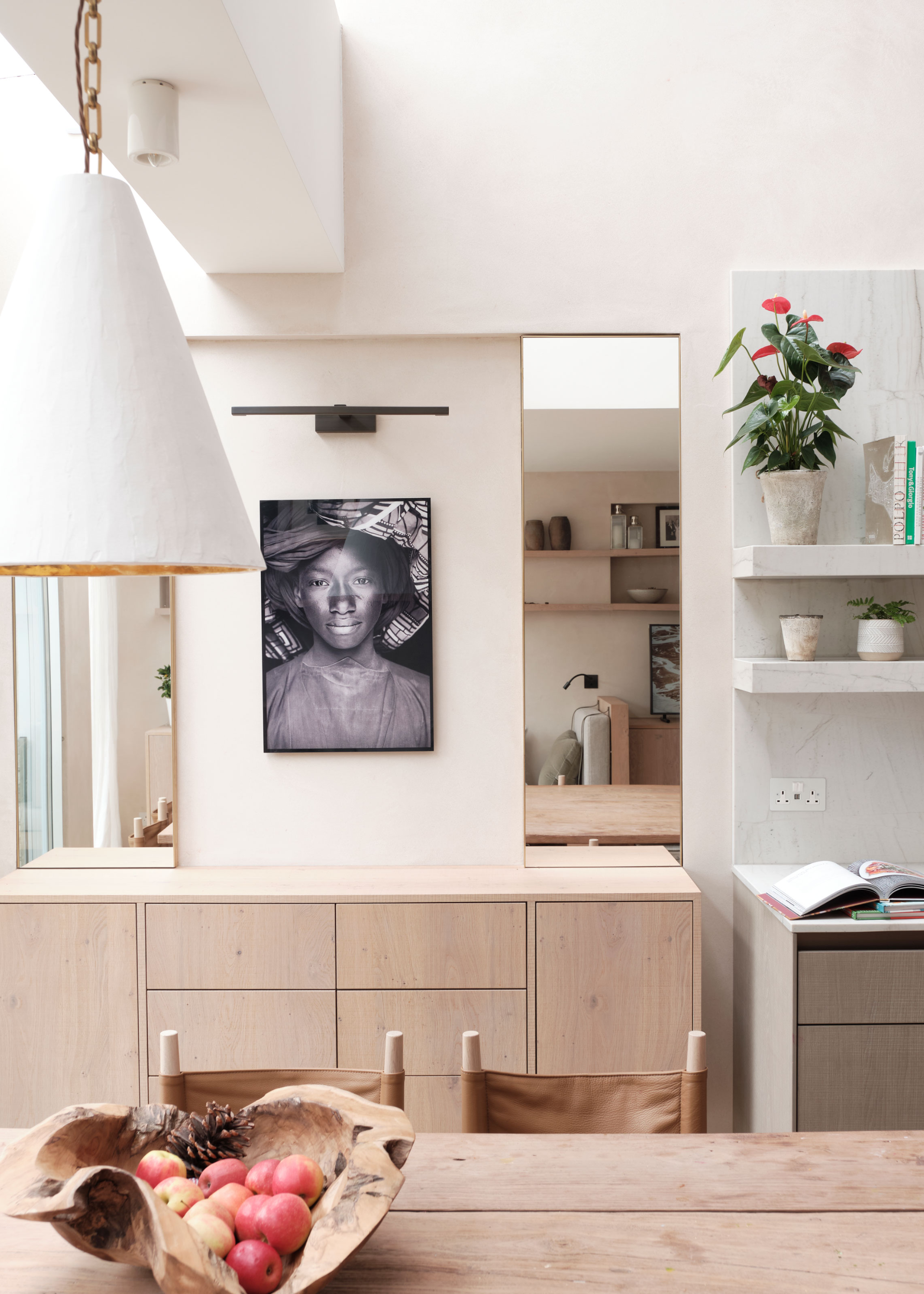 A kitchen with artwork hanging as well as a view of the dining table that has a bowl of fruit in the middle