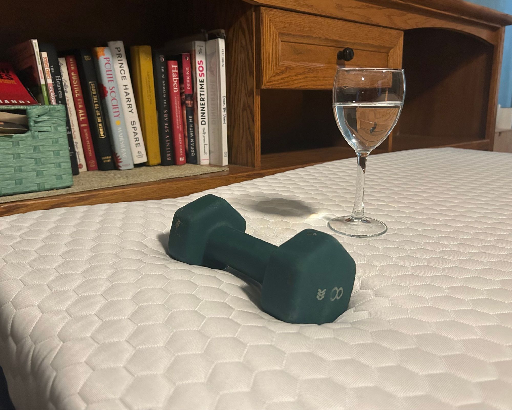 Testing the Brooklyn Bedding copperflex mattress topper with a wine glass of water, dark green dumbbell weight, and a bookshelf behind.