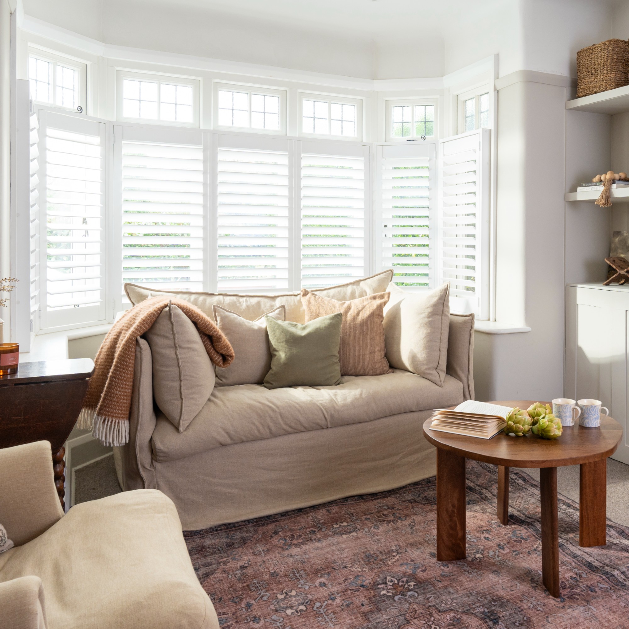 A white living room with a two-seater beige linen sofa with loose covers, a round coffee table and a vintage-style rug