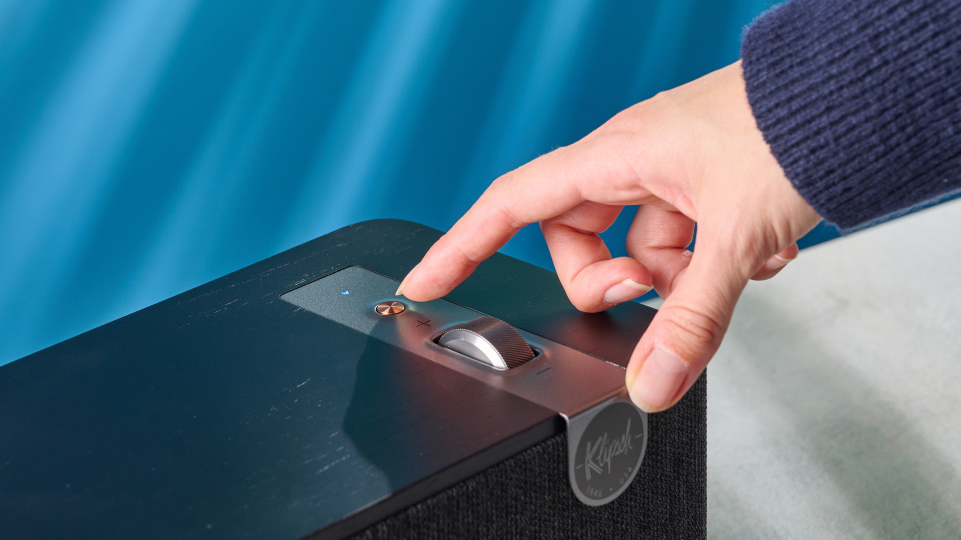 Klipsch The One Plus Bluetooth speaker in matte black photographed in front of a blue background.