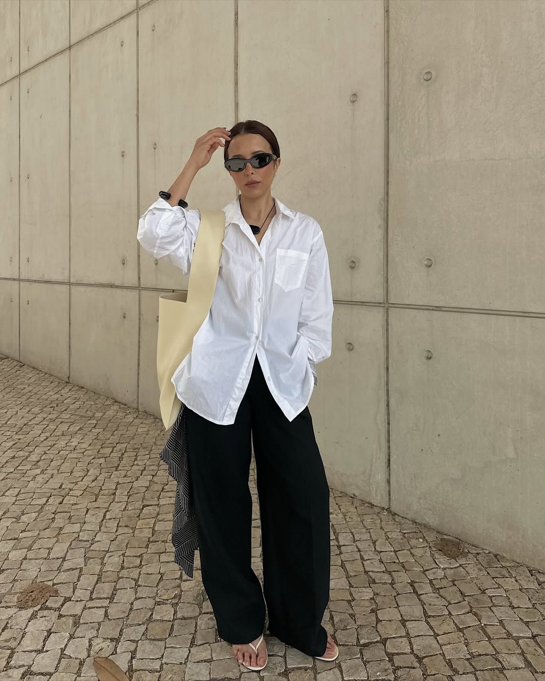 @deborabrosa wears a white linen shirt, black linen trousers, a yellow leather tote and white flip-flops
