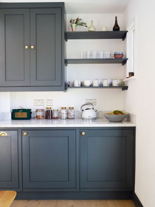 dark blue kitchen cupboards with marble style countertops and infill shelves